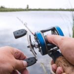 hand with baitcasting reel and rod against river