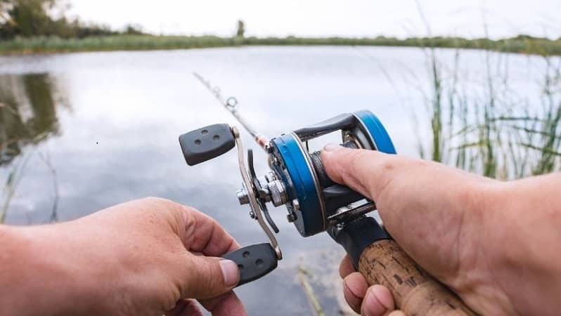 hand with baitcasting reel and rod against river