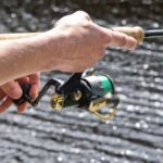 hands on spinning reel and fishing rod by the water