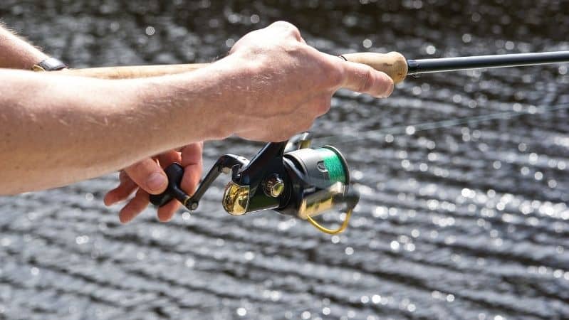 hands on spinning reel and fishing rod by the water