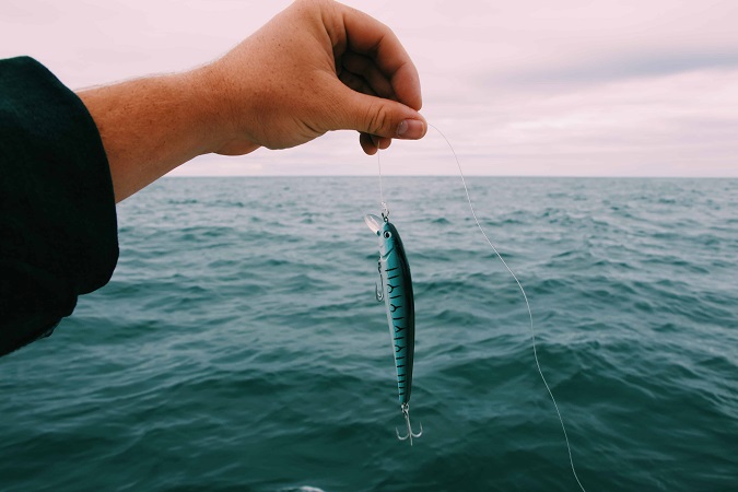 hand holding fish lure against open sea