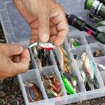 hand choosing lures from tackle box